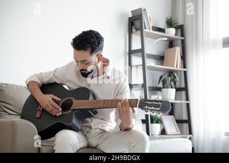 Handsome man sitting on sofa at home and playing guitar Stock Photo