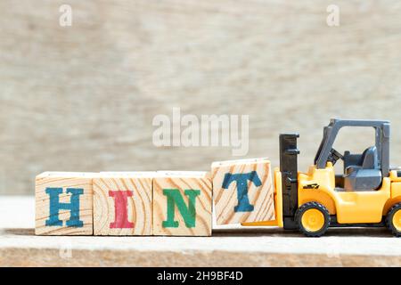 Toy forklift hold letter block t to complete word hint on wood background Stock Photo