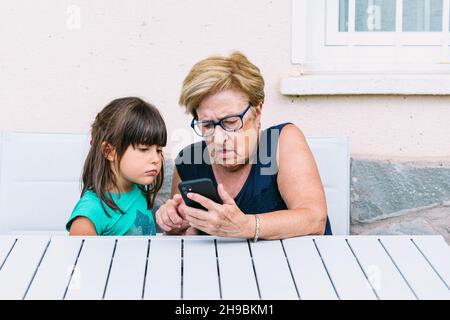 Grandmother and granddaughter consulting the mobile on a terrace. Family, grandchildren, grandparents and technology concept. Stock Photo