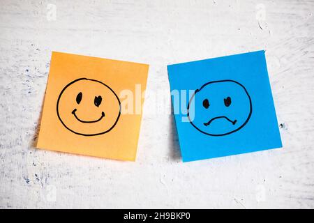 Happy and sad faces hand drawn on sticky notes on painted wall Stock Photo