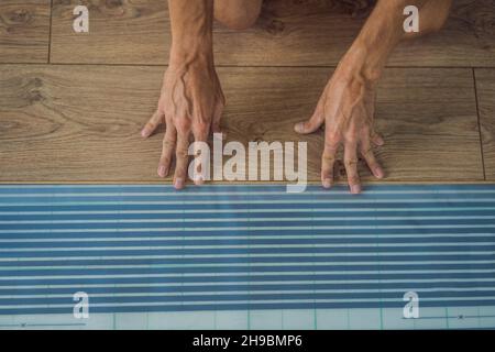 Man installing new wooden laminate flooring on a warm film floor. Infrared floor heating system under laminate floor Stock Photo