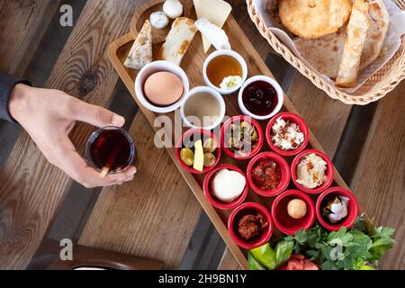 Delicious traditional turkish breakfast with hand holding turkish tea on the wooden table. Stock Photo