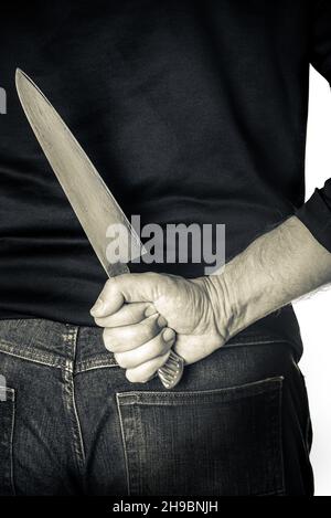 Person hairy skin chef holding kitchen knife hidden behind the back Stock Photo