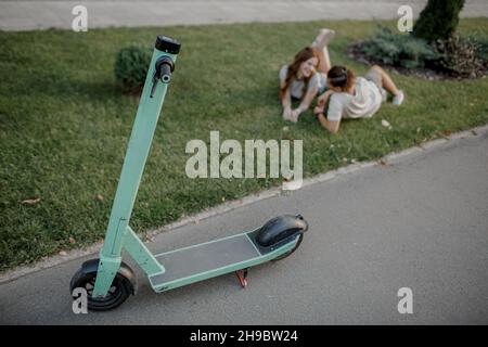 Charming girl and an attractive guy are lying on the grass and talking. Couple is using eco transport Stock Photo