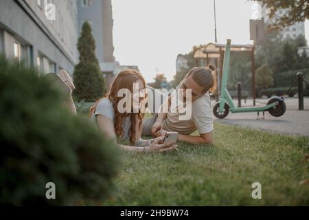 Charming girl and an attractive guy are lying on the grass with smart phone. Couple is using eco transport Stock Photo