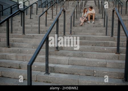 Charming couple is sitting on the stairs outside and having nice conversation Stock Photo