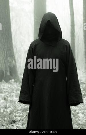 Death in a black hoodie mantle in forest mystery fog. Horror style fear