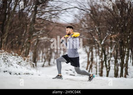Sportsman doing lunges and holding weights in nature at snowy winter day. Bodybuilding, healthy habits, winter fitness Stock Photo