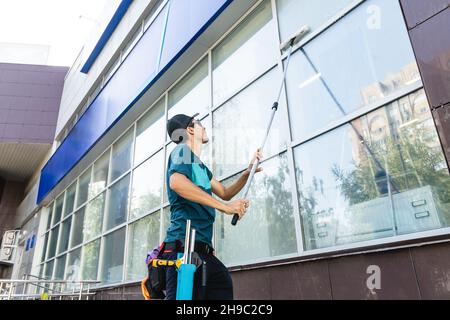 An employee of a professional cleaning service in overalls washes the facade and windows with special devices Stock Photo