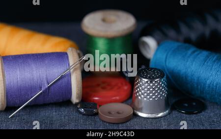 Thread, needle, thimble, buttons are on gray fabric. Closeup Stock Photo