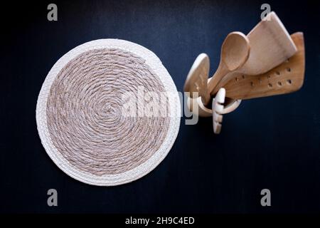 set of wooden wooden spoon spatula kitchen utensils next to wicker knitted empty placemat on black isolated background Stock Photo