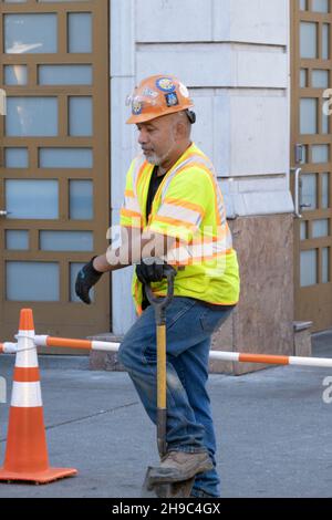 A construction worker in a helmet and safety vest takes a brief break. In Williamsburg, Brooklyn, New York City. Stock Photo