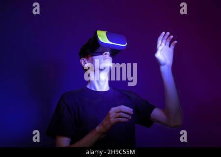 Young man in a VR helmet interacts with objects in virtual reality in neon colors. Stock Photo