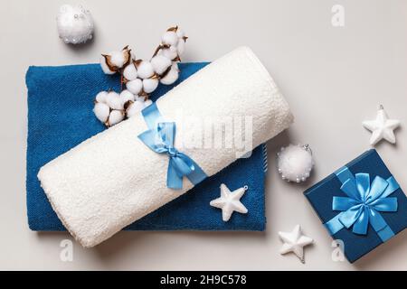White and blue terry towels with a bow on a gray background. Gift box cotton branch with Christmas decorations. Stock Photo