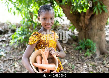 Beautiful young black african girl with some giant carrots in her pumpkin bowl on her way to the village market Stock Photo