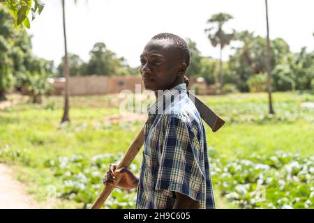 Thoughtful young black African farmer with a hoe on his shoulder staring at the horizon Stock Photo