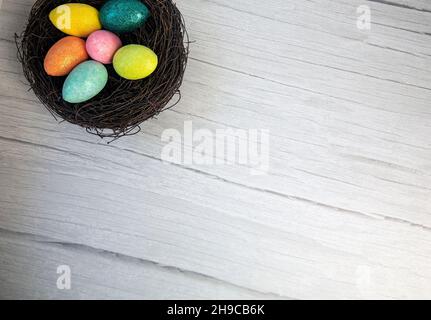Colorful Easter Egg Nest with Extra White or Gray Wood Board Background for room or space for copy, text, words. A flat lay with square crop, Happy Stock Photo