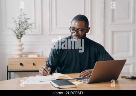 Focused young african american businessman writing down notes in notebook while working in office Stock Photo