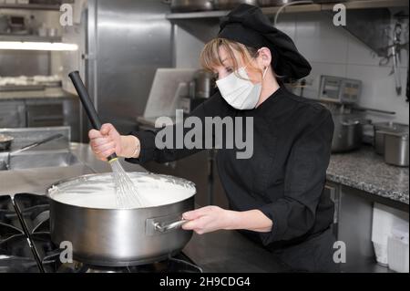 Health protection, safety and pandemic concept - Female chef cook wearing a protective face mask while working at restaurant kitchen. High quality photo Stock Photo