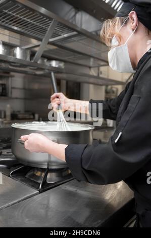 Health protection, safety and pandemic concept - Female chef cook wearing a protective face mask while working at restaurant kitchen. High quality photo Stock Photo
