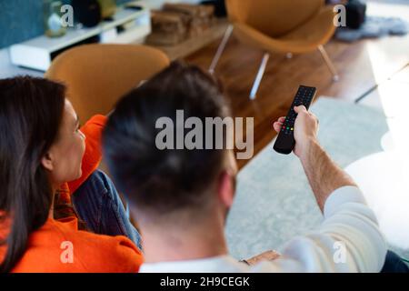 Rear view shot of a woman and man relaxing on the sofa together while man holding a remote controller in his hand. Stock Photo