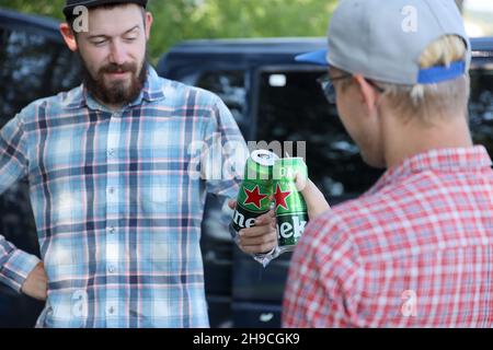 KHARKOV, UKRAINE - JULY 31, 2021: Green tin cans of Heineken pale lager beer in men hands outdoors Stock Photo