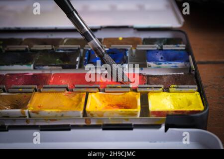 The artist applies red watercolor paint on an art brush. Drawing with watercolors in a home art studio. Stock Photo