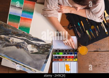 The artist applies yellow watercolor paint on an art brush. Drawing with watercolors in a home art studio. Stock Photo