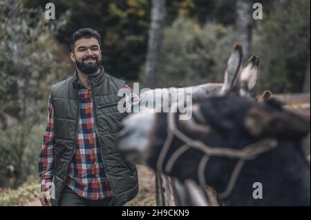 Bearded farmer standing near the donkey in a cattle-pen Stock Photo