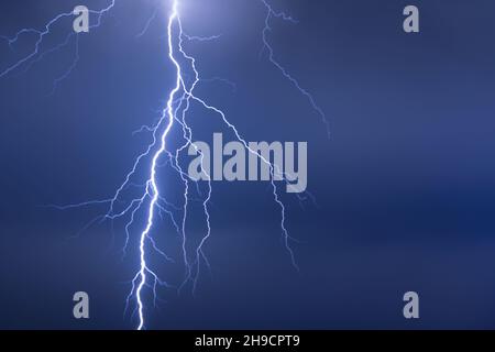 Lightning or thunderbolt in night storm in dramatic blue light Stock Photo