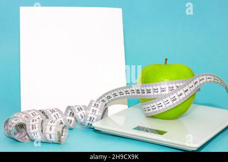 centimeter tape around green apple on scales isolated on blue background with place for text. concept of proper nutrition, diet Stock Photo