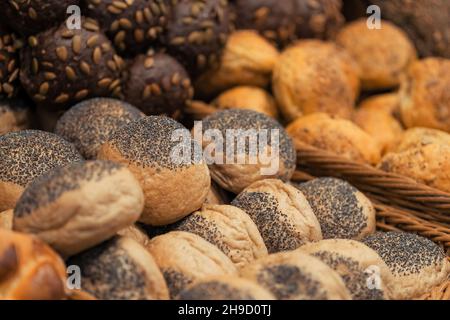 Close-up photo of breakfast lines of  rye buns with sunflower seeds and white wheat buns with poppy seeds in wooden trays at the hotel restaurant. Stock Photo