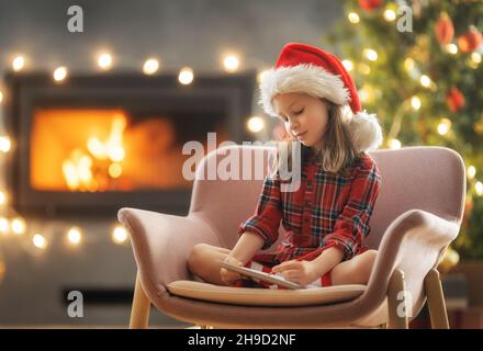 Merry Christmas and Happy Holidays! Cute little child girl is writing the letter to Santa Claus near tree indoors. Stock Photo