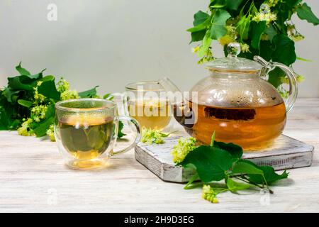 Teapot and two cups of tea with a linden tree on a wooden table. Healing tea. Stock Photo