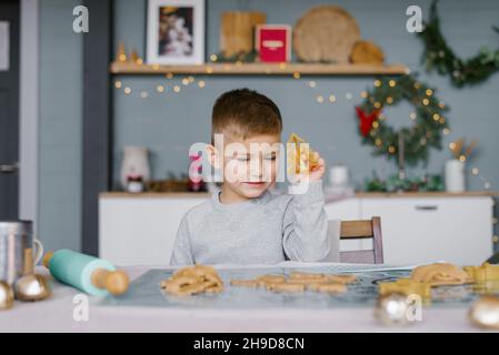 A cute little boy is sitting at the table and preparing Christmas cookies. Family vacation at home during the holidays. New Year and Christmas.