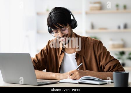 Joyful middle eastern guy attending webinar, using laptop, taking notes Stock Photo