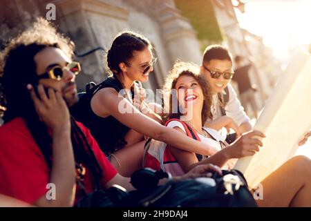 Friends exploring old city fortress. Having a good time at street. Sitting on stairs. Stock Photo