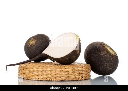 One half and two whole ripe juicy black radishes on a straw tray, close-up, isolated on white. Stock Photo