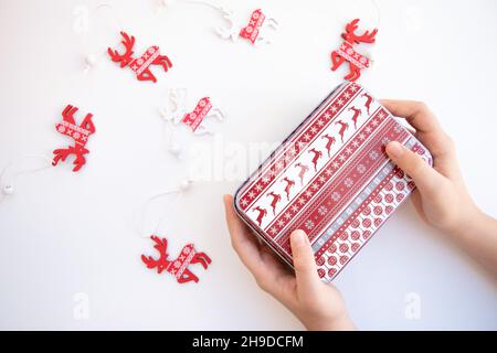 A girl holding a christmas gift in her hands, with a white and red reindeer pattern, against a white background with reindeer decorations on Stock Photo