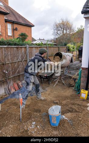 A Builder making cement in a cement mixer, example of a labourer doing manual labour; building work,  on a building site, England UK