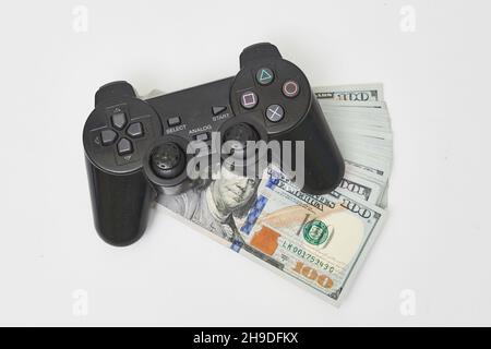 Game console controller and pile of money. Gamepad and us dollars. Wireless game pad on dollar bills. Concept of game addiction, spending money on Stock Photo