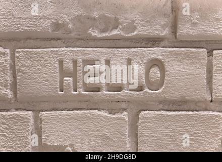 Background texture depicting a wall made with white painted cement bricks and the english word hello carved in center. Stock Photo