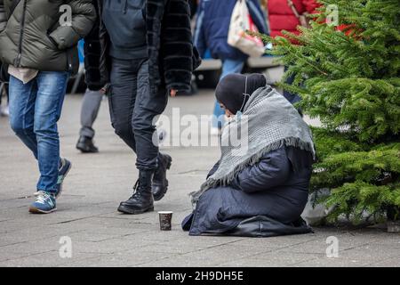 Essen, North Rhine-Westphalia, Germany - Beggar woman sits on the pavement in the pedestrian zone during the Corona pandemic at Christmas time. Passer Stock Photo