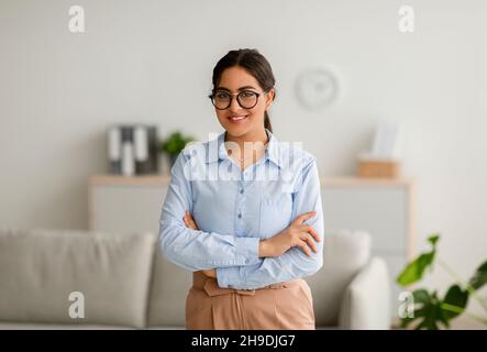 Professional psychotherapy. Portrait of young successful arab female psychologist posing with folded arms in office Stock Photo