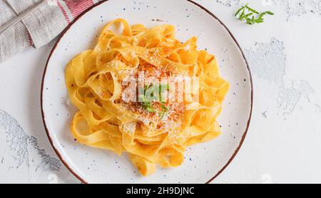 Fettuccine pasta with traditional Italian Passat sauce and parmesan cheese in light plate on old white concrete background. Top view.