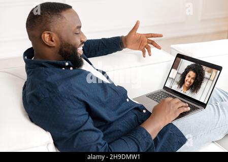 Happy African-American guy making video call to charming biracial woman on the laptop screen, talking with a girlfriend online, using dating app. Black guy using laptop for video connection Stock Photo
