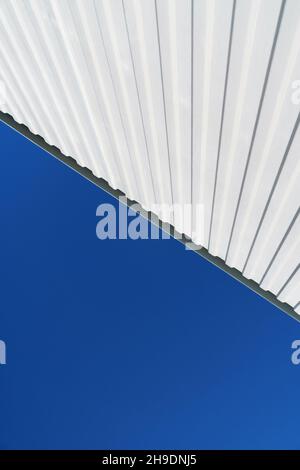 Textured white metal structures diagonally against a blue sky. Abstraction in buildings Stock Photo