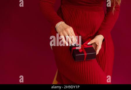 Woman wearing red opened box with present, pulling red stripe. Stock Photo