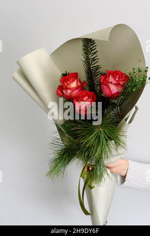Beautiful present of red tender blooming bouquet. Various fresh flowers and pine branches in white paper. Gift idea for Valentine's day. Christmas bou Stock Photo
