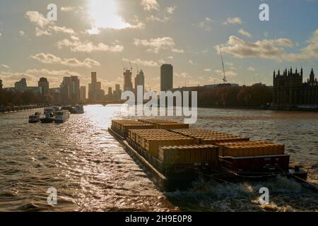 Barge on River Thames against low bright sun in blue sky with clouds Stock Photo